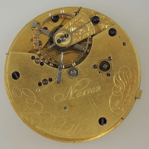 May include: Close-up of the inner workings of a gold pocket watch with the inscription "N&deg; 6169" and "Robt.  B.  Ball" visible on the face.