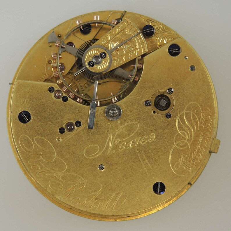 May include: Close-up of the inner workings of a gold pocket watch with the inscription "N&deg; 6169" and "Robt.  B.  Ball" visible on the face.