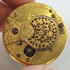 Op de afbeelding: Close-up van een gouden zakhorloge met ingewikkelde gravures en de inscriptie "J. Latham, Manchester".