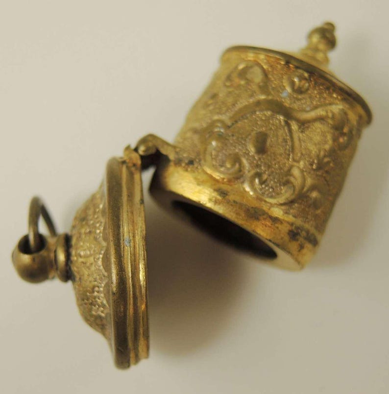 May include: A gold-toned metal locket with an ornate design. The locket is open, revealing an empty interior.