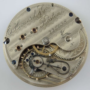 K&ouml;nnte beinhalten: Nahaufnahme eines silbernen Taschenuhrwerks mit der Inschrift "E. Howard & Co. Boston" und der Seriennummer "225098". Das Werk ist justiert und hat ein dekoratives Design.