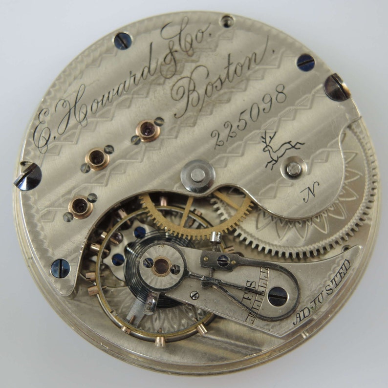K&ouml;nnte beinhalten: Nahaufnahme eines silbernen Taschenuhrwerks mit der Inschrift "E. Howard & Co. Boston" und der Seriennummer "225098". Das Werk ist justiert und hat ein dekoratives Design.