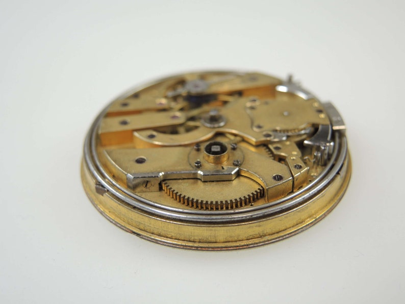 Op de afbeelding: Close-up van een gouden zakhorloge-uurwerk met ingewikkelde tandwielen en een zilveren ring aan de rand.