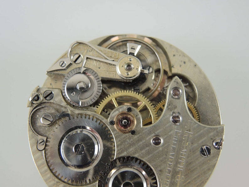 May include: Close-up view of the inner workings of a silver pocket watch. The watch face is visible with the text "G.S. SMITH PHILADELPHIA" printed on it.