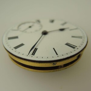 Pu&ograve; includere: Primo piano del quadrante di un orologio da tasca vintage. Il quadrante bianco presenta numeri romani neri, un piccolo quadrante dei secondi e lancette nere. La cassa dell'orologio &egrave; dorata con una fascia marrone scuro.