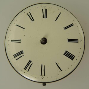 May include: Cream-colored clock face with black Roman numerals and a small central post. The face has a black outer ring and small dots marking the minutes. The clock face shows signs of age.