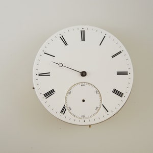 May include: A white pocket watch face featuring black Roman numerals and hands. A smaller subdial is at the bottom. The watch face has a vintage aesthetic, with a classic design. A great addition to any watch collection.