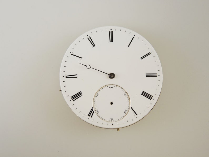 May include: A white pocket watch face featuring black Roman numerals and hands. A smaller subdial is at the bottom. The watch face has a vintage aesthetic, with a classic design. A great addition to any watch collection.