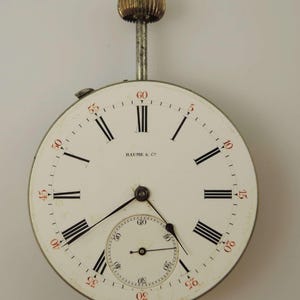 Puede incluir: Un reloj de bolsillo blanco con marcadores de hora romanos negros y agujas negras. La esfera del reloj tiene un subdial m&aacute;s peque&ntilde;o con agujas negras y marcas negras. La esfera del reloj tambi&eacute;n tiene el texto "BAUME & C" impreso en &eacute;l. El reloj tiene una caja plateada y una perilla dorada en la parte superior.