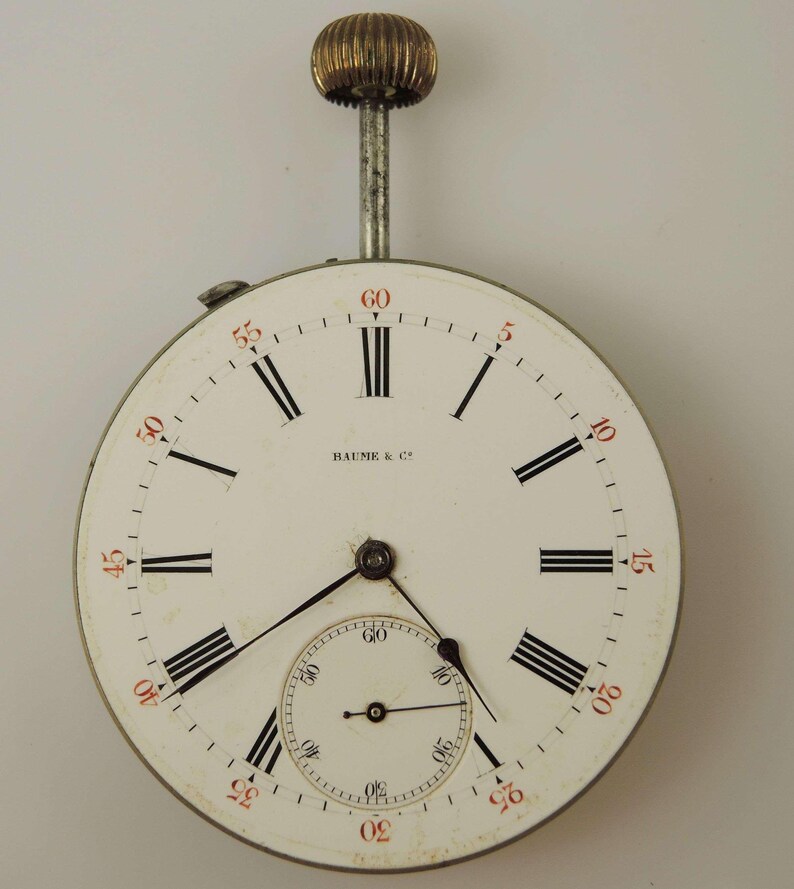 Puede incluir: Un reloj de bolsillo blanco con marcadores de hora romanos negros y agujas negras. La esfera del reloj tiene un subdial m&aacute;s peque&ntilde;o con agujas negras y marcas negras. La esfera del reloj tambi&eacute;n tiene el texto "BAUME & C" impreso en &eacute;l. El reloj tiene una caja plateada y una perilla dorada en la parte superior.