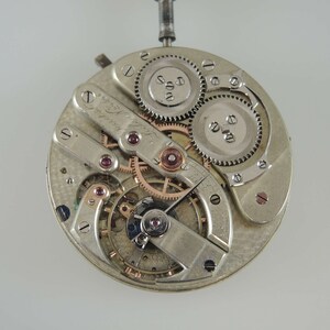 May include: Close-up of a silver watch movement with intricate gears and a rose gold finish. The movement is visible through a clear case back.