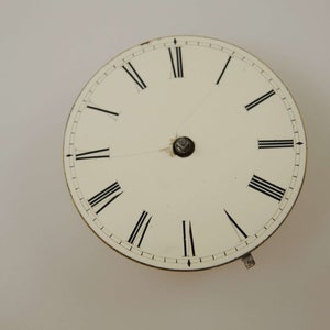 May include: A white clock face with black Roman numeral hour markers and black minute markers. The clock face is circular and has a silver center.