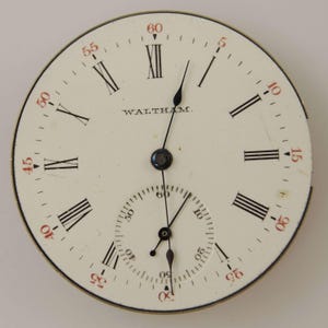 May include: A vintage watch face with a cream-colored background. Black Roman numerals mark the hours, with red numerals for the minutes. The word "WALTHAM" is printed in black. The watch face has two black hands and a smaller subdial.