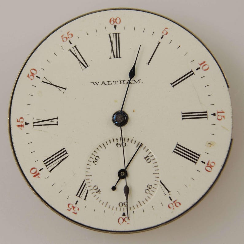 May include: A vintage watch face with a cream-colored background. Black Roman numerals mark the hours, with red numerals for the minutes. The word "WALTHAM" is printed in black. The watch face has two black hands and a smaller subdial.