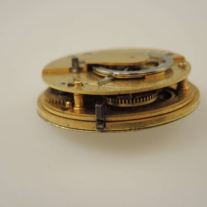 May include: Close-up of a gold-colored pocket watch mechanism with intricate gears and a silver-colored winding stem.