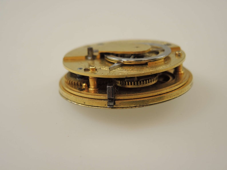 May include: Close-up of a gold-colored pocket watch mechanism with intricate gears and a silver-colored winding stem.