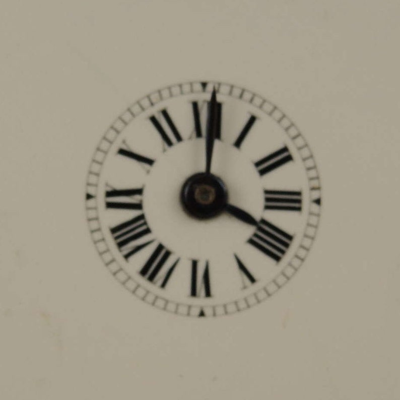 May include: A white clock face with black Roman numeral markings and black hands. The clock face is surrounded by a black ring with small black markings.