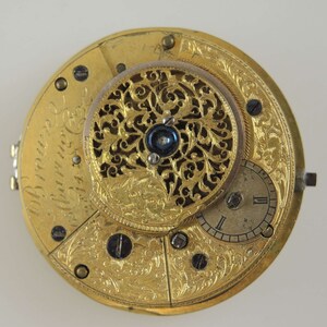 Puede incluir: Un reloj de bolsillo de oro con un dise&ntilde;o intrincado grabado. La esfera del reloj es visible y presenta n&uacute;meros romanos. La inscripci&oacute;n "John Brown London" es visible en la esfera del reloj.