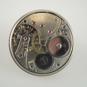 K&ouml;nnte beinhalten: Nahaufnahme eines silbernen Taschenuhrwerks mit der Aufschrift "W. L. Forge & Valentine Chicago, Ill. 6 Adj. Patent Applied For" und der Nummer "900127".