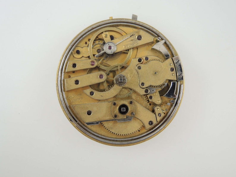 Op de afbeelding: Close-up van een goudkleurig zakhorloge-uurwerk met ingewikkelde tandwielen en hendels. Het horloge is gedemonteerd en de interne werking is zichtbaar.