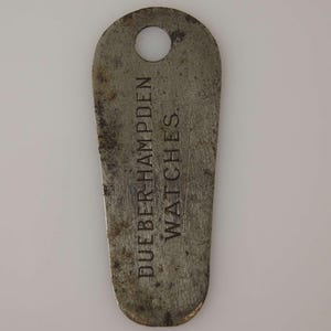 Könnte beinhalten: Ein silberner Schlüsselanhänger mit dem eingravierten Text "Dueber Hampden Watches".