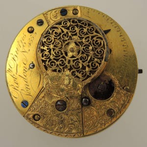 Puede incluir: Primer plano de un movimiento de reloj de oro vintage. El mecanismo del reloj presenta intrincados grabados florales y una cubierta de filigrana decorativa. El texto "Robt. Burgess London" est&aacute; inscrito en la superficie dorada. Est&eacute;tica cl&aacute;sica y antigua.