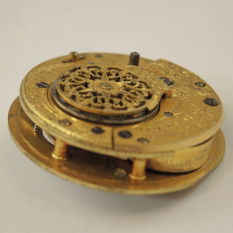 May include: A gold pocket watch with intricate details on the face and a decorative openwork design on the back. The watch is in a disassembled state, showing the inner workings.