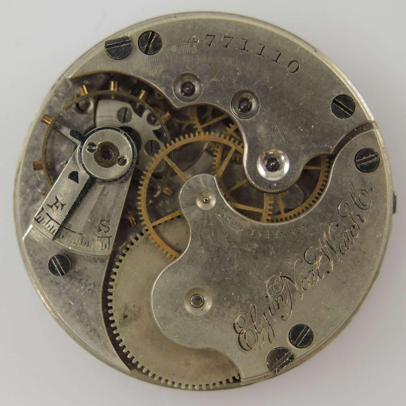 May include: Close-up of a vintage watch movement, showcasing intricate gears, screws, and a balance wheel. The metal components are silver-toned with gold-colored gears. The text "Elgin Nat'l Watch Co." is visible.