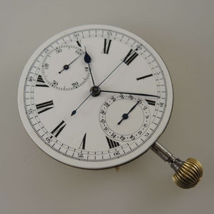 May include: A white pocket watch with a silver case and black Roman numeral hour markers. The watch has a chronograph function with a smaller dial at the bottom and a second hand that extends from the center of the watch face.