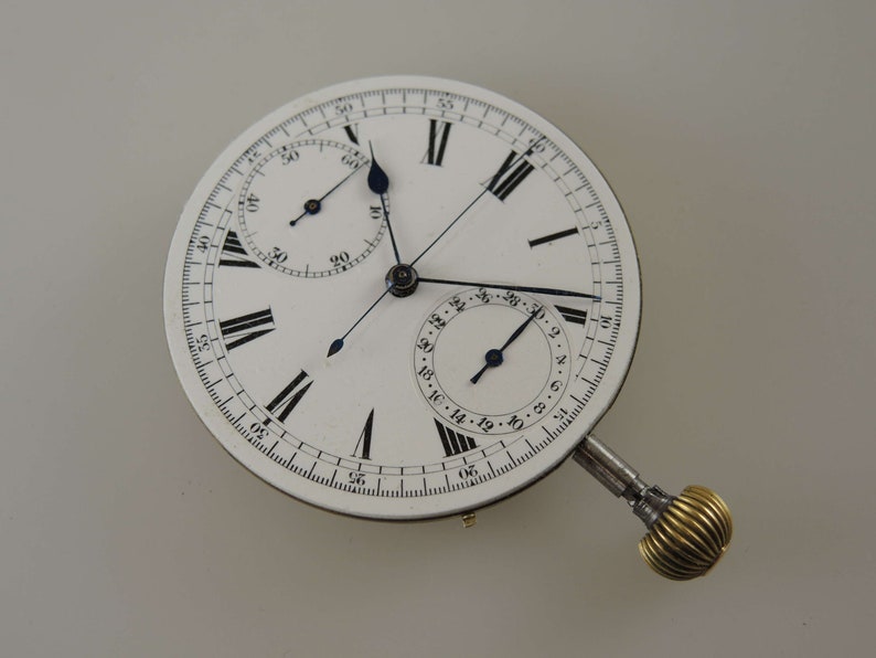 May include: A white pocket watch with a silver case and black Roman numeral hour markers. The watch has a chronograph function with a smaller dial at the bottom and a second hand that extends from the center of the watch face.