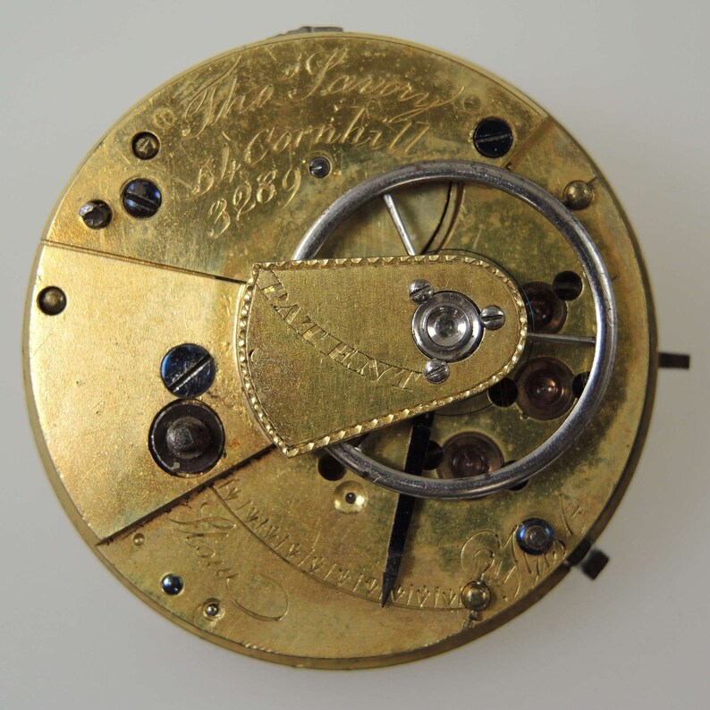 Puede incluir: Primer plano de un movimiento de reloj de bolsillo de color dorado con un mecanismo de cuerda plateado. La esfera del reloj est&aacute; inscrita con "Mr. Jarvey 56 Cornhill 3289" y "Patent Inv't".