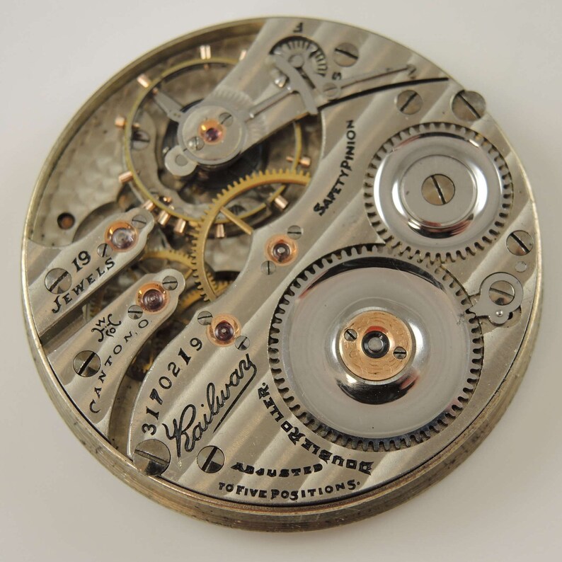 K&ouml;nnte beinhalten: Nahaufnahme eines silbernen Taschenuhrwerks mit dem Text "19 Jewels", "Canton, O", "3170219", "Railwar", "Safety Pinion", "Roller Double", "Adjusted to Five Positions."