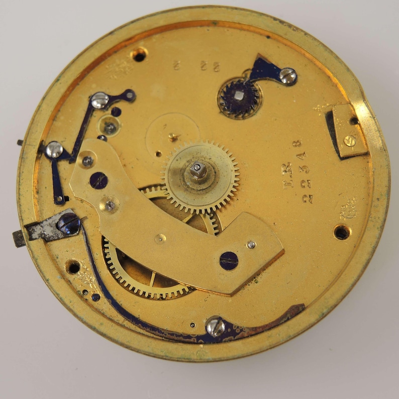 May include: A detailed view of a gold-coloured watch mechanism, showcasing gears, levers, and screws. The circular movement features the numbers "2 2" and "2348". The intricate design is set against a plain white backdrop.