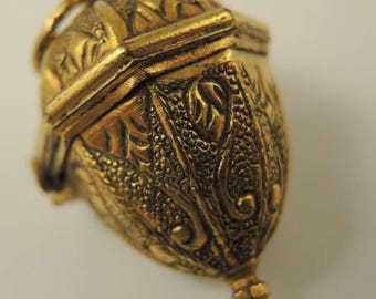 May include: A gold-toned acorn-shaped locket with an intricate floral design. The locket opens and closes with a hinged lid.