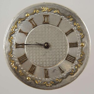 May include: A detailed view of a silver pocket watch face featuring Roman numerals and a patterned central area. Gold-coloured embellishments and a decorative border are present. The hands are black.