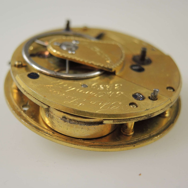 Puede incluir: Un movimiento de reloj de bolsillo de oro con una tapa parcialmente abierta. El movimiento est&aacute; inscrito con el texto "J.C. & S.  London  No. 1120".
