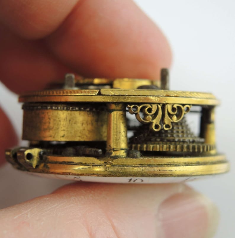 May include: Close-up side view of a gold-toned pocket watch movement with intricate details. The watch face is visible with the number "10" printed on it.