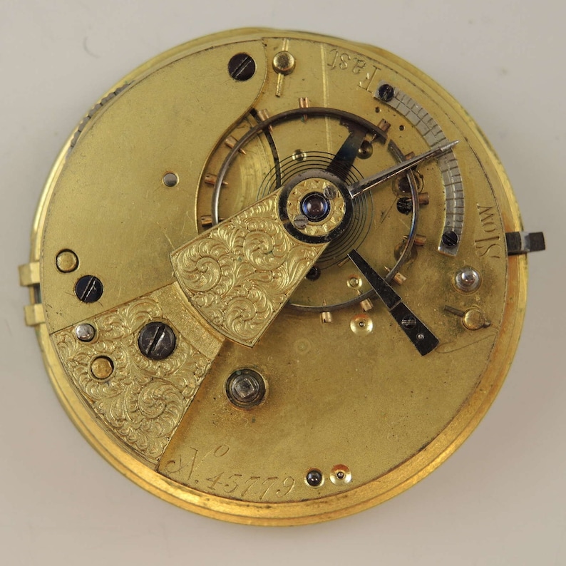 May include: Close-up of a gold pocket watch movement with intricate engravings. The watch face features the text "Slow" and "Fast" and the number "145779".