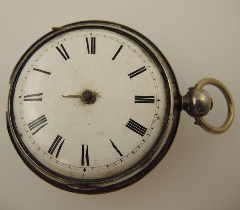 May include: A vintage pocket watch with a white face and black Roman numerals. The watch has a silver-colored casing and a gold-colored ring for attaching a chain. The hands are black and the watch shows the time as approximately 2:40.