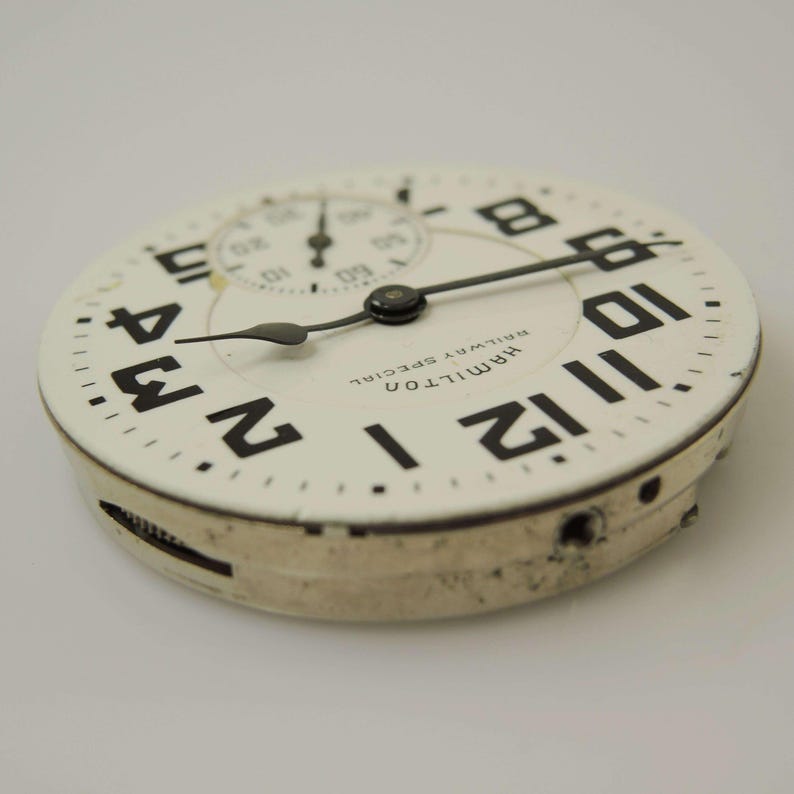 Pu&ograve; includere: Primo piano di un quadrante di orologio vintage con sfondo bianco e numeri neri. Il quadrante dell'orologio ha un quadrante secondario pi&ugrave; piccolo e lancette nere. Le parole "HAMILTON RAILWAY SPECIAL" sono stampate sul quadrante. Il quadrante &egrave; leggermente usurato.