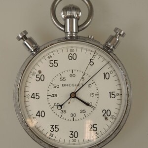 May include: A silver stopwatch with a white face and black hands. The face has markings for seconds, minutes, and hours. The stopwatch is made by Breguet.