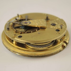 May include: Close-up of a gold-toned pocket watch movement with intricate gears and a chain. The watch is disassembled and the inner workings are visible.