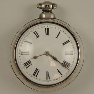 Könnte beinhalten: Eine silberne Taschenuhr mit römischen Ziffern für die Stunden und einem weißen Zifferblatt. Die Uhr hat ein silbernes Gehäuse und eine silberne Kette.