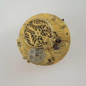 K&ouml;nnte beinhalten: Ein goldfarbenes Taschenuhrwerk mit aufwendigen floralen Gravuren. Das Zifferblatt der Uhr ist mit r&ouml;mischen Ziffern und einem kleinen, kreisf&ouml;rmigen Zifferblatt mit den Zahlen 5, 10, 15, 20, 25, 30 sichtbar.