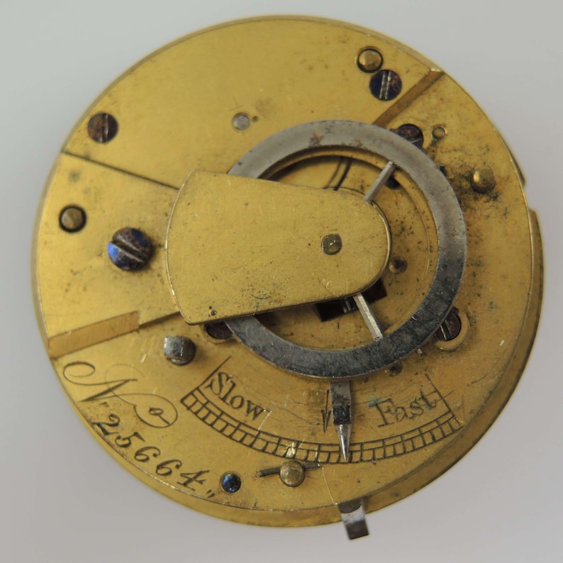 May include: Close-up of a vintage watch movement with a gold-colored plate. The mechanism features a silver-colored balance wheel and a regulator labeled "Slow" and "Fast". The serial number "25664" is also visible.