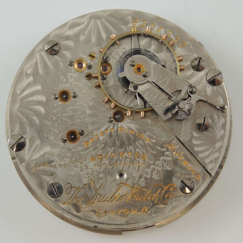 May include: Close-up of the back of a silver pocket watch with a gold-colored inscription that reads "The Huber Watch Co. Canton, O." and "Safety Pinion Adjusted For Five Positions."