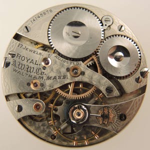 May include: Close-up of a vintage watch movement with intricate gears and components. The watch mechanism features the text "ROYAL A.W.W.Co. WALTHAM, MASS." and "17 JEWELS ADJUSTED." The serial number "14145878" is also visible.