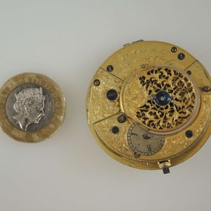 Puede incluir: Un reloj de bolsillo de oro con grabados intrincados y un centro azul. La esfera del reloj es visible y tiene marcas de n&uacute;meros romanos.
