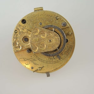 K&ouml;nnte beinhalten: Eine goldene Taschenuhr mit aufwendigen Gravuren und einem sichtbaren Getriebemechanismus. Das Zifferblatt der Uhr ist mit dem Text "J. Flowr" beschriftet.