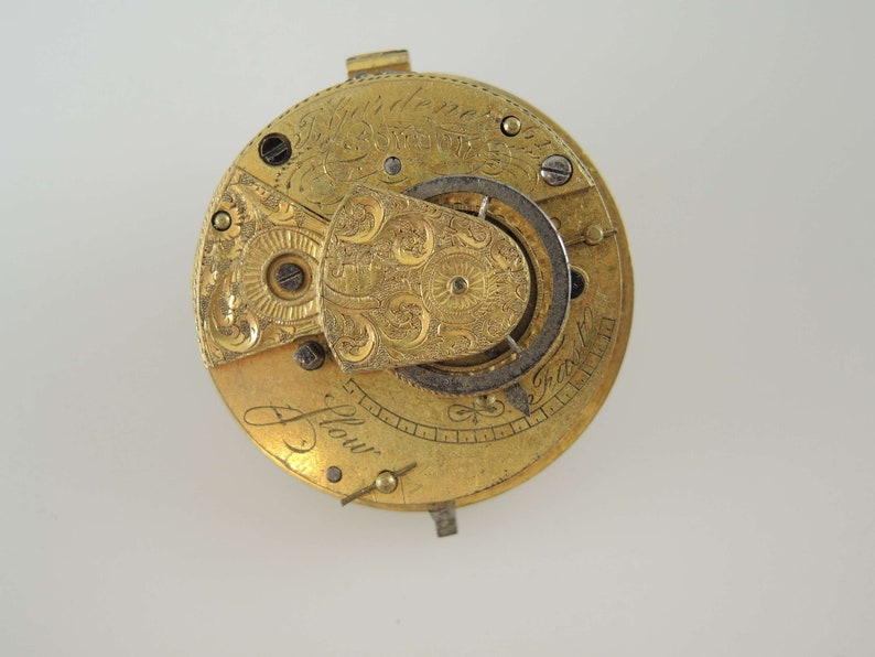 K&ouml;nnte beinhalten: Eine goldene Taschenuhr mit aufwendigen Gravuren und einem sichtbaren Getriebemechanismus. Das Zifferblatt der Uhr ist mit dem Text "J. Flowr" beschriftet.